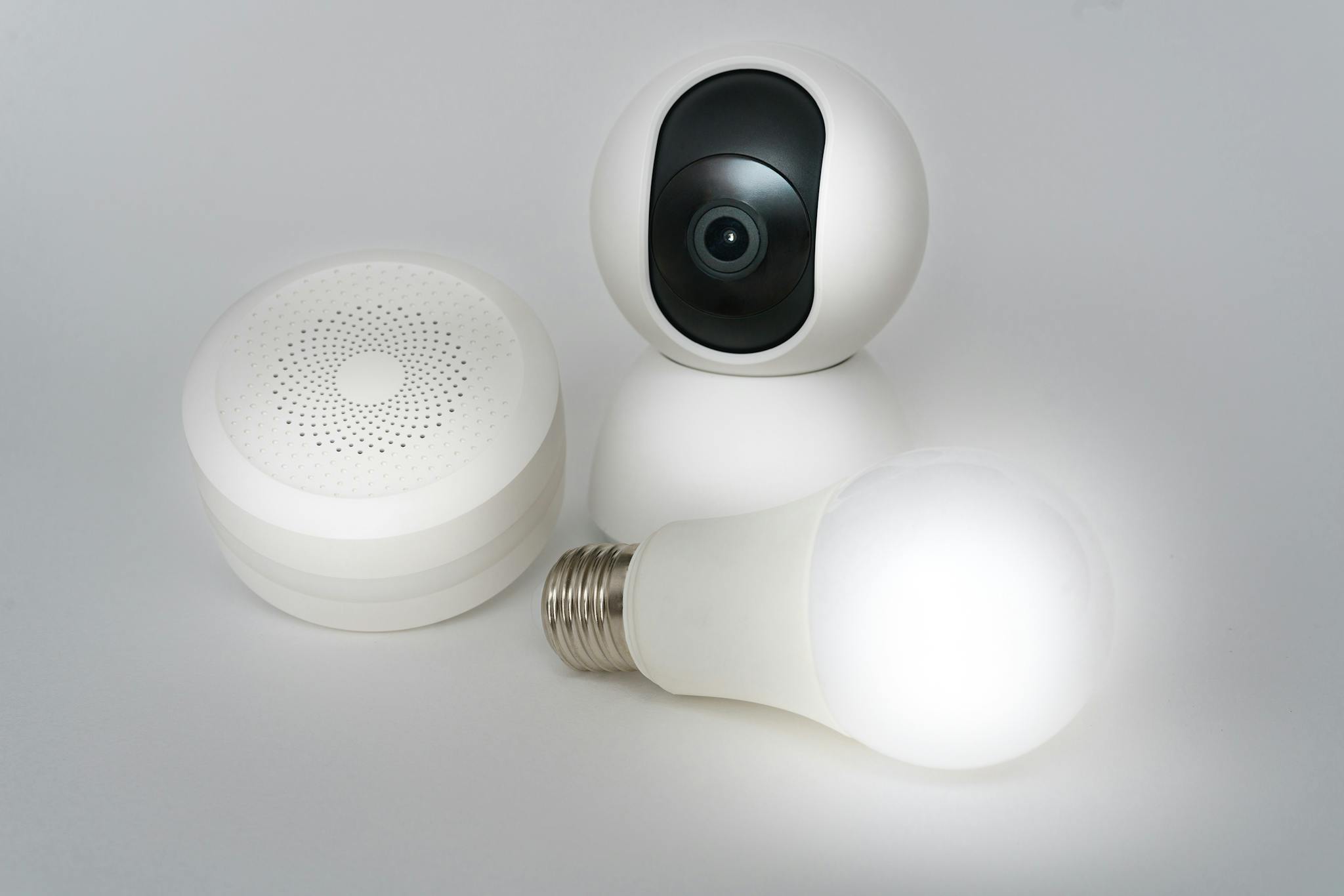 A set of smart home devices including a camera, speaker, and lightbulb on a white background.