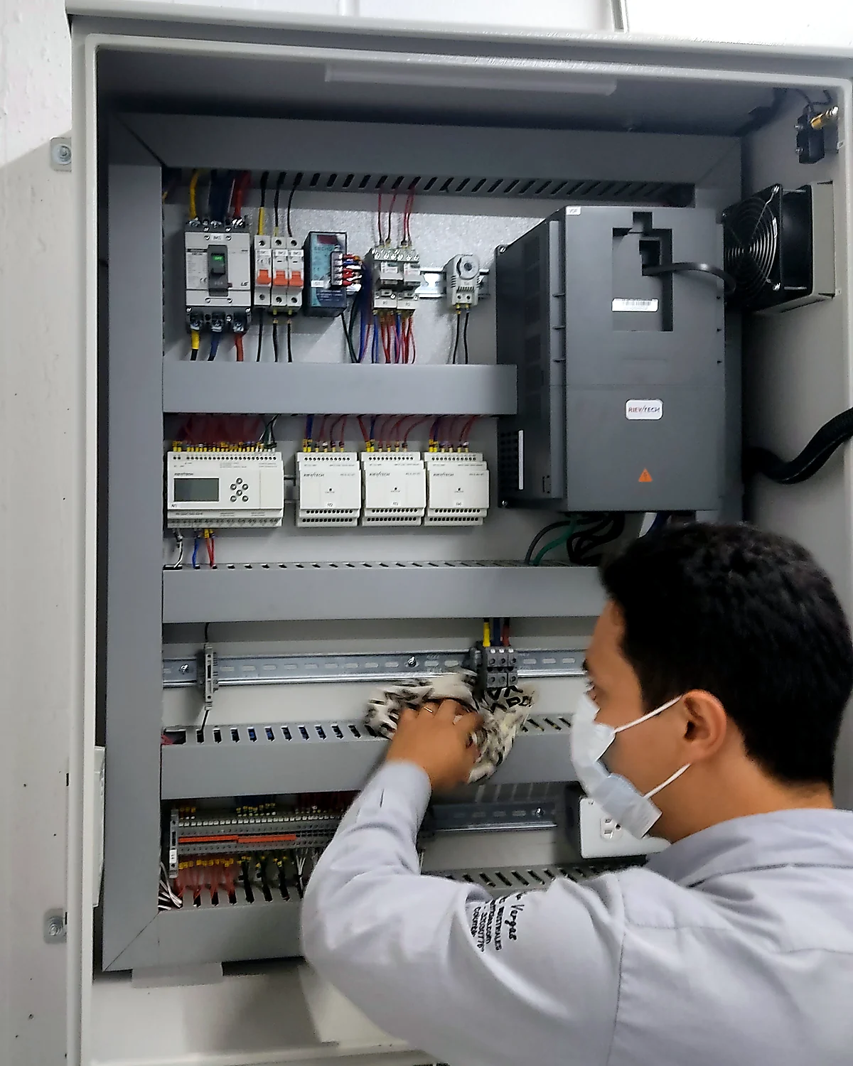 Técnico de SOLINTECK conectando y marcando borneras en un tablero de control con PLC, módulos de expansión y variador de velocidad